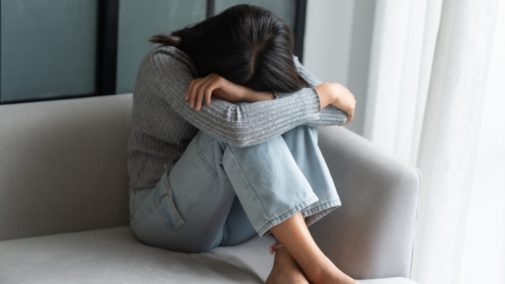 Mulher sentada no sofá, encolhida, de cabeiça baixa sobre os joelhos. Como perseverar na quaresma em meio a dificuldades sérias.