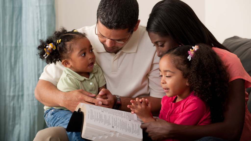 Pai e Mãe, com duas crianças, lendo a bíblia. Livros Infantis Cristãos para Ler com os Filhos Durante a Preparação para a Páscoa.